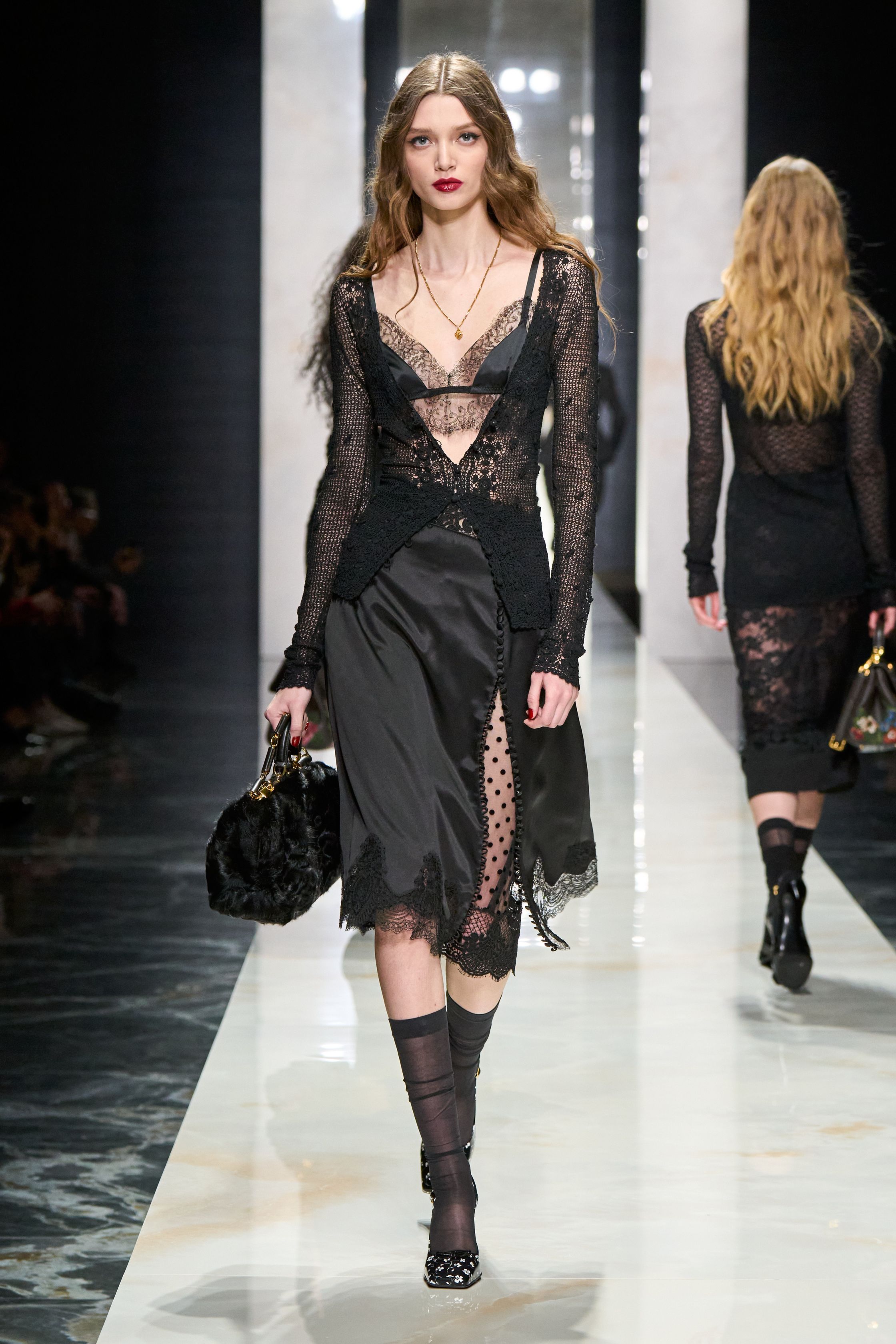 Dolce & Gabbana在本季回归品牌标志性的性感意大利美学，通过黑色蕾丝、修身西装与透视礼服塑造极具戏剧张力的女性形象。系列以黑色为核心色调，结合紧身胸衣结构、透明蕾丝裙与宽肩西装，形成刚柔并济的视觉语言。皮草外套与复古帽饰则增添奢华氛围，使整体造型在性感与优雅之间保持平衡，呈现出典型的意大利电影般的华丽气质-顽石频道趋势研究